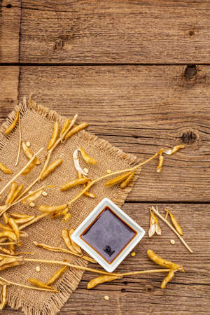 Ripe dry soybeans in pods and dark soy sauce. Cultivated organic agricultural crop, traditional healthy ingredients in oriental food. Vintage sackcloth, wooden boards background, copy space, top viewの写真素材