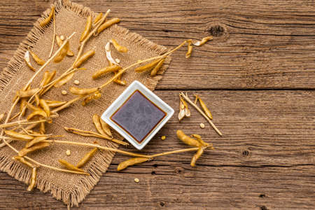 Ripe dry soybeans in pods and dark soy sauce. Cultivated organic agricultural crop, traditional healthy ingredients in oriental food. Vintage sackcloth, wooden boards background, copy space, top viewの写真素材
