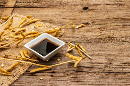 Ripe dry soybeans in pods and dark soy sauce. Cultivated organic agricultural crop, traditional healthy ingredients in oriental food. Vintage sackcloth, wooden boards background, copy spaceの写真素材