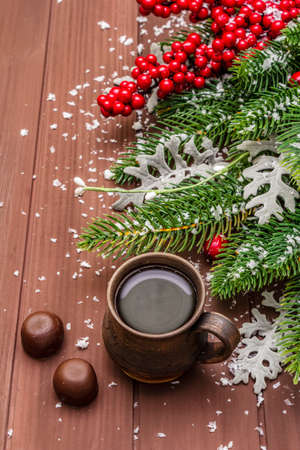 Christmas hot coffee background. New Year fir tree, dog rose, fresh leaves, chocolate candies and artificial snow. Wooden boards backdrop, close upの写真素材