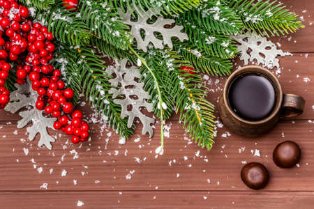 Christmas hot coffee background. New Year fir tree, dog rose, fresh leaves, chocolate candies and artificial snow. Wooden boards backdrop, top view, close upの写真素材