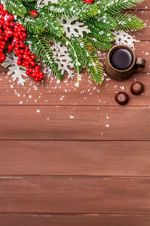 Christmas hot coffee background. New Year fir tree, dog rose, fresh leaves, chocolate candies and artificial snow. Wooden boards backdrop, copy space, top viewの写真素材
