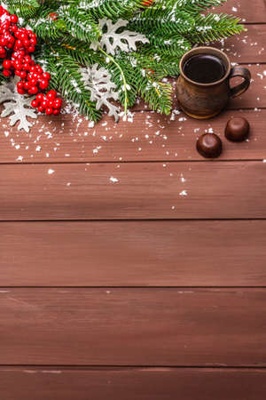 Christmas hot coffee background. New Year fir tree, dog rose, fresh leaves, chocolate candies and artificial snow. Wooden boards backdrop, copy spaceの写真素材