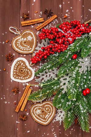 Christmas background. New Year fir tree, dog rose, fresh leaves, crocheted ginger cookies hearts, spices and artificial snow. Wooden boards backdrop, top view, close upの写真素材