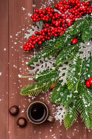 Christmas hot coffee background. New Year fir tree, dog rose, fresh leaves, chocolate candies and artificial snow. Wooden boards backdrop, top viewの写真素材