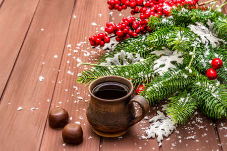 Christmas hot coffee background. New Year fir tree, dog rose, fresh leaves, chocolate candies and artificial snow. Wooden boards backdrop, copy space, close upの写真素材