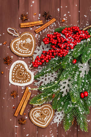 Christmas background. New Year fir tree, dog rose, fresh leaves, crocheted ginger cookies hearts, spices and artificial snow. Wooden boards backdrop, top view, close upの写真素材
