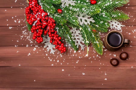 Christmas hot coffee background. New Year fir tree, dog rose, fresh leaves, chocolate candies and artificial snow. Wooden boards backdrop, copy space, top viewの写真素材