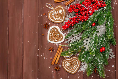Christmas background. New Year fir tree, dog rose, fresh leaves, crocheted ginger cookies hearts, spices and artificial snow. Wooden boards backdrop, copy space, top viewの写真素材