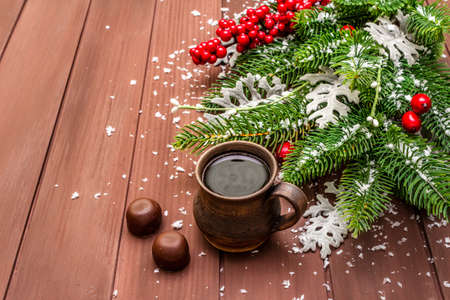 Christmas hot coffee background. New Year fir tree, dog rose, fresh leaves, chocolate candies and artificial snow. Wooden boards backdrop, copy spaceの写真素材