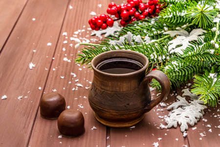 Christmas hot coffee background. New Year fir tree, dog rose, fresh leaves, chocolate candies and artificial snow. Wooden boards backdrop, copy space, close upの写真素材