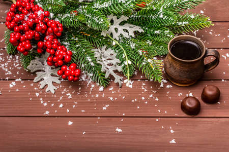 Christmas hot coffee background. New Year fir tree, dog rose, fresh leaves, chocolate candies and artificial snow. Wooden boards backdrop, copy spaceの写真素材