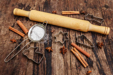 Christmas baking background, bake ware, spices, cookie cutters - stars, angel and fir tree, sieve, sugar powder and a rolling pin. Old wooden boards, copy spaceの写真素材