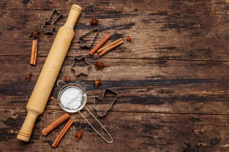 Christmas baking background, bake ware, spices, cookie cutters - stars, angel and fir tree, sieve, sugar powder and a rolling pin. Old wooden boards, copy space, top viewの写真素材