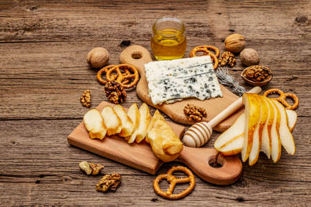 Cheese plate antipasti with smoked and blue cheese, crackers, honey, walnuts and ripe pear. Traditional snack recipe idea. Wooden boards background, copy spaceの写真素材