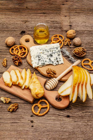 Cheese plate antipasti with smoked and blue cheese, crackers, honey, walnuts and ripe pear. Traditional snack recipe idea. Wooden boards background, copy spaceの写真素材
