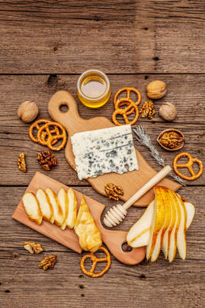 Cheese plate antipasti with smoked and blue cheese, crackers, honey, walnuts and ripe pear. Traditional snack recipe idea. Wooden boards background, top view, close upの写真素材
