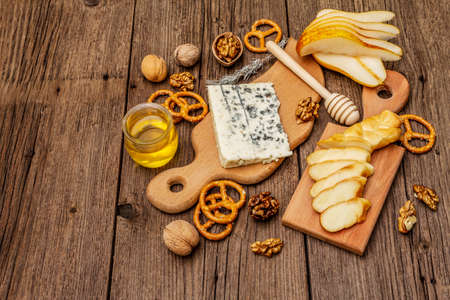Cheese plate antipasti with smoked and blue cheese, crackers, honey, walnuts and ripe pear. Traditional snack recipe idea. Wooden boards background, copy spaceの写真素材