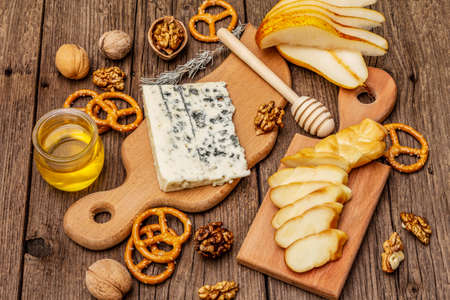 Cheese plate antipasti with smoked and blue cheese, crackers, honey, walnuts and ripe pear. Traditional snack recipe idea. Wooden boards background, close upの写真素材