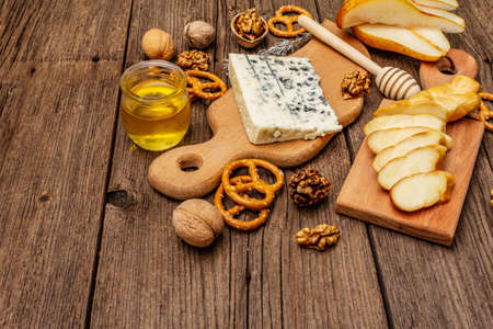 Cheese plate antipasti with smoked and blue cheese, crackers, honey, walnuts and ripe pear. Traditional snack recipe idea. Wooden boards background, copy spaceの写真素材