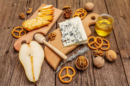 Cheese plate antipasti with smoked and blue cheese, crackers, honey, walnuts and ripe pear. Traditional snack recipe idea. Wooden boards background, close upの写真素材