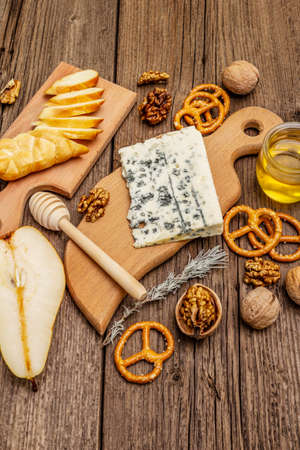 Cheese plate antipasti with smoked and blue cheese, crackers, honey, walnuts and ripe pear. Traditional snack recipe idea. Wooden boards background, close upの写真素材