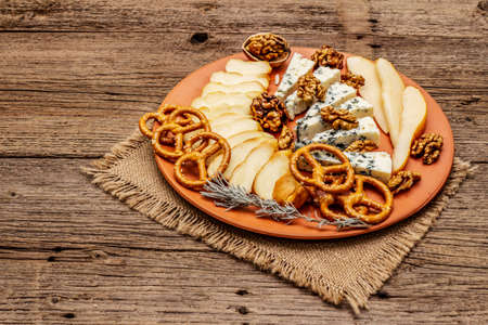 Cheese plate antipasti with smoked and blue cheese, crackers, honey, walnuts and ripe pear. Traditional snack recipe idea. Wooden boards background, copy spaceの写真素材