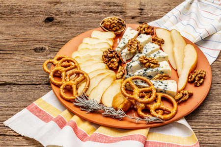 Cheese plate antipasti with smoked and blue cheese, crackers, honey, walnuts and ripe pear. Traditional snack recipe idea. Wooden boards background, copy space, close upの写真素材
