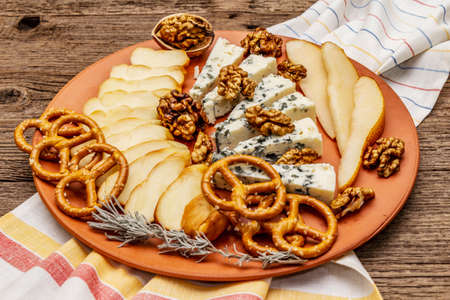 Cheese plate antipasti with smoked and blue cheese, crackers, honey, walnuts and ripe pear. Traditional snack recipe idea. Wooden boards background, close upの写真素材