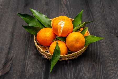 Fresh ripe tangerines with leaves in basket. New Year or Christmas wooden background. Festive good mood concept, copy spaceの写真素材