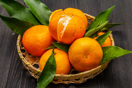 Fresh ripe tangerines with leaves in basket. New Year or Christmas wooden background. Festive good mood concept, close upの写真素材