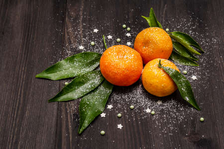 Fresh ripe tangerines with leaves and sprinkles. New Year or Christmas wooden background covered artificial snow. Festive good mood concept, close upの写真素材