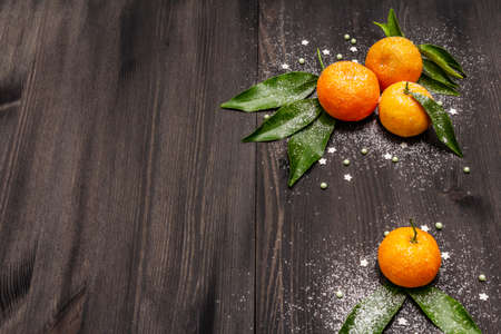 Fresh ripe tangerines with leaves and sprinkles. New Year or Christmas wooden background covered artificial snow. Festive good mood concept, copy spaceの写真素材