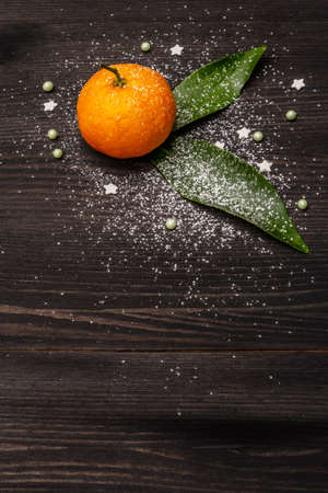 Fresh ripe tangerines with leaves and sprinkles. New Year or Christmas wooden background covered artificial snow. Festive minimalistic concept, copy space, close upの写真素材