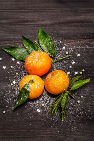 Fresh ripe tangerines with leaves and sprinkles. New Year or Christmas wooden background covered artificial snow. Festive good mood concept, top view, close upの写真素材