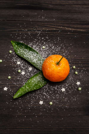 Fresh ripe tangerines with leaves and sprinkles. New Year or Christmas wooden background covered artificial snow. Festive minimalistic concept, copy space, top view, close upの写真素材