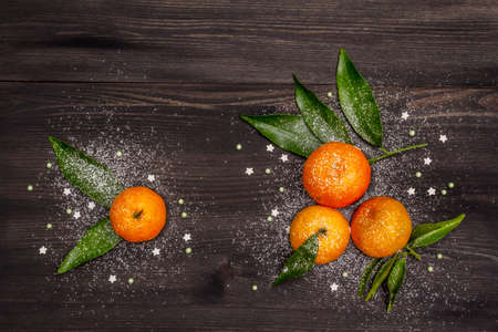 Fresh ripe tangerines with leaves and sprinkles. New Year or Christmas wooden background covered artificial snow. Festive good mood concept, copy space, top viewの写真素材