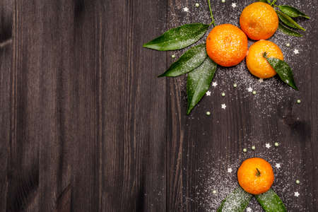 Fresh ripe tangerines with leaves and sprinkles. New Year or Christmas wooden background covered artificial snow. Festive good mood concept, copy space, top viewの写真素材