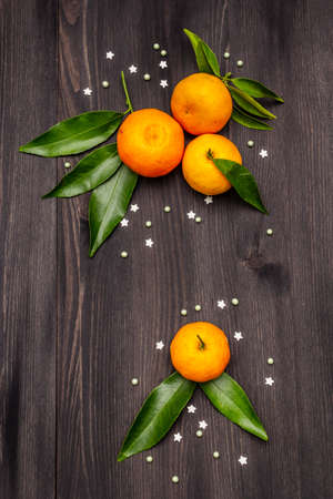 Fresh ripe tangerines with leaves and sprinkles. New Year or Christmas wooden background. Festive good mood concept, copy space, top viewの写真素材