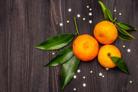 Fresh ripe tangerines with leaves and sprinkles. New Year or Christmas wooden background. Festive good mood concept, copy space, top view, close upの写真素材