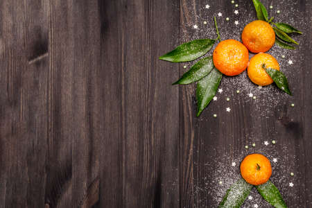 Fresh ripe tangerines with leaves and sprinkles. New Year or Christmas wooden background covered artificial snow. Festive good mood concept, copy space, top viewの写真素材