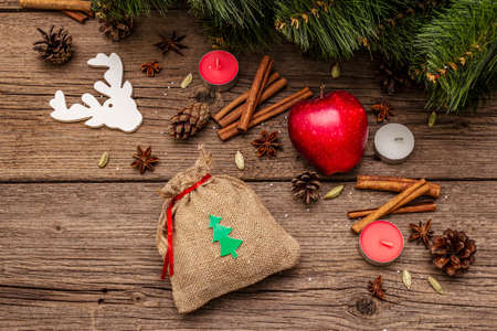 Spirit Christmas background. Gift in sack, New Year tree, apple, candles, spices, deer, cones. Nature decorations, vintage wooden boards, top view, copy spaceの写真素材