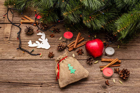 Spirit Christmas background. Gift in sack, New Year tree, apple, candles, spices, deer, cones. Nature decorations, vintage wooden boards, top viewの写真素材