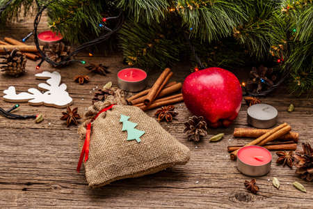 Spirit Christmas background. Gift in sack, New Year tree, apple, candles, spices, deer, cones. Nature decorations, vintage wooden boards, close upの写真素材