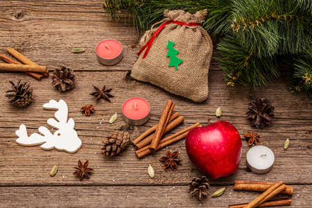 Spirit Christmas background. Gift in sack, New Year tree, apple, candles, spices, deer, cones. Nature decorations, vintage wooden boards, close upの写真素材