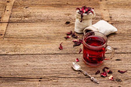 Hot hibiscus tea. Dry petals, linen sacks. Healthy food and self-care concept. Old wooden boards backgrounds, copy spaceの写真素材