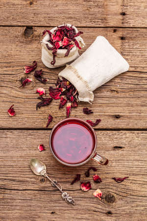 Hot hibiscus tea. Dry petals, linen sacks. Healthy food and self-care concept. Old wooden boards backgrounds, close up, top viewの写真素材