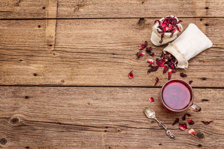 Hot hibiscus tea. Dry petals, linen sacks. Healthy food and self-care concept. Old wooden boards backgrounds, copy space, top viewの写真素材