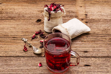 Hot hibiscus tea. Dry petals, linen sacks. Healthy food and self-care concept. Old wooden boards backgrounds, copy space, close upの写真素材
