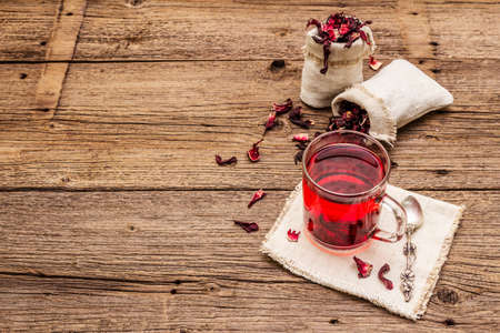 Hot hibiscus tea. Dry petals, linen sacks. Healthy food and self-care concept. Old wooden boards backgrounds, copy spaceの写真素材